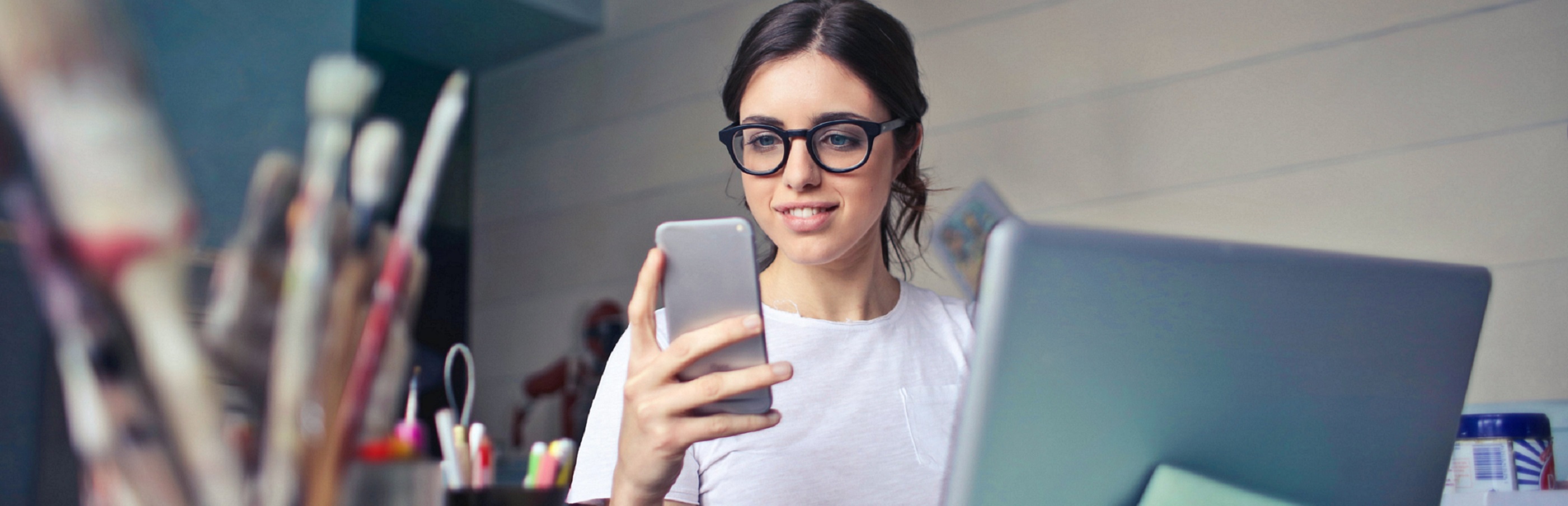 Woman in art studio working on laptop and looking at her mobile phone